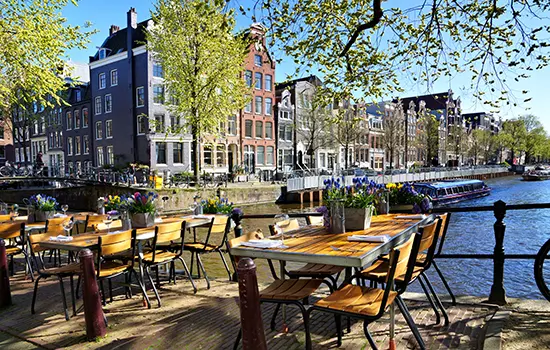 Restaurant tables lining the beautiful canals of Amsterdam under blue skies during springtime, Netherlands